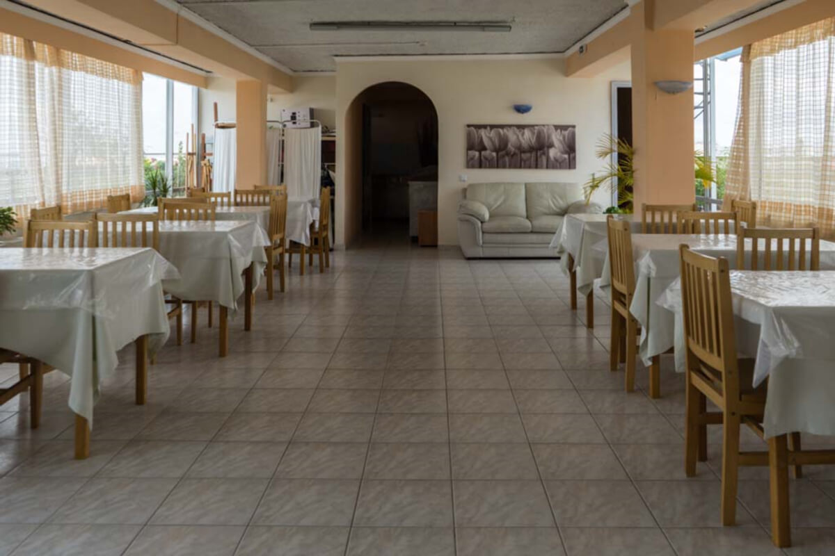 Αίθουσα εστίασης με στρωμένα τραπέζια, ξύλινες καρέκλες, καναπέ και τοξωτό πέρασμα στο βάθος